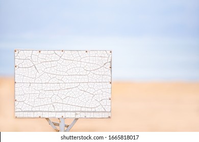A White Sign With Cracks On A Background Of Beige Sand And Sky. The Concept Of Desperate Travel, Unexpected Adventures, And Renting Housing In Southern Countries, Real Estate Sales, Advertising, Ads.