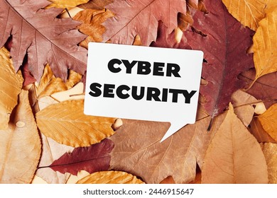 A white sign with the word Cybersecurity written on it is placed on top of a pile of autumn leaves