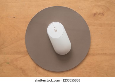 White And Silver Wireless Mouse On A Gray Round Leather Mouse Pad On A Wooden Surface.