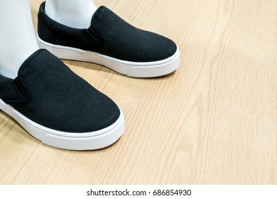 White skin mannequin model feet wearing black canvas casual shoe standing on wooden floor texture at clothing store. - Powered by Shutterstock