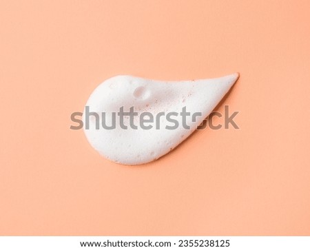 White skincare cleansing foam on peach background. Soap, shampoo or shower gel foam texture, close-up, top view
