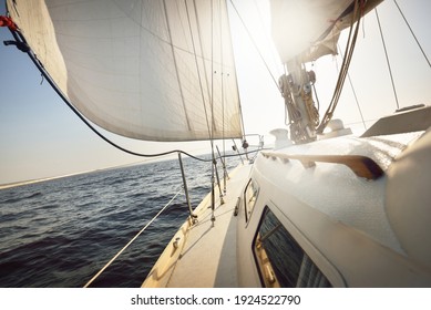 White sloop rigged yacht sailing in an open sea at sunset. Clear sky. A view from the deck to the bow, mast, sails. Transportation, travel, cruise, sport, recreation, leisure activity, racing, regatta