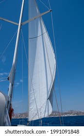 White Sloop Rigged Yacht Sailing In Open Calm Ocean, Blue Sky Background, Sunny Day. Sailboat Deck, Bow, Mast And Sails Closeup View. Aegean Sea Sailing, Summer Holidays In Cyclades Islands, Greece