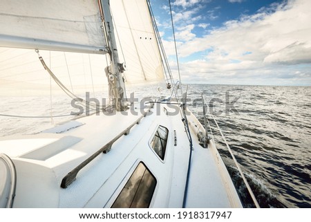 White sloop rigged yacht sailing in an open sea on a clear day. A view from the deck to the bow. Cumulus clouds. Transportation, travel, cruise, sport, recreation, leisure activity, racing, regatta