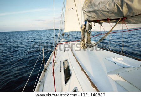 White sloop rigged yacht sailing in the sea at sunset. Clear sky. A view from the deck to the bow, mast, sails. Transportation, travel, cruise, sport, recreation, leisure activity, racing, regatta