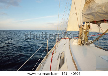 White sloop rigged yacht sailing in the sea at sunset. Clear sky. A view from the deck to the bow, mast, sails. Transportation, travel, cruise, sport, recreation, leisure activity, racing, regatta