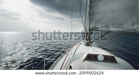 White sloop rigged yacht sailing at sunset. Clear sky after the storm. View from the deck to the bow, mast, sails. Transportation, travel, cruise, sport, recreation, leisure activity, racing, regatta