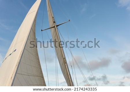 White sloop rigged yacht sailing in an open sea on a clear day. White sails against blue sky with glowing clouds after the rain. Transportation, travel, cruise, sport, recreation, racing, regatta