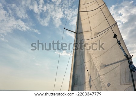 White sloop rigged yacht sails against cloudy blue sky. Sailing in an open sea. Summer vacations, leisure activity, sport and recreation, private wessel concepts