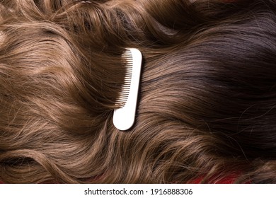 A white small plastic comb on a wavy brown long shiny synthetic extensions of synthetic brown hair wig
