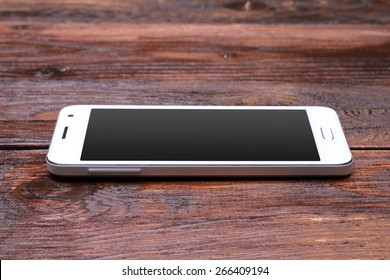 White smart phone with blank screen lying on wooden table