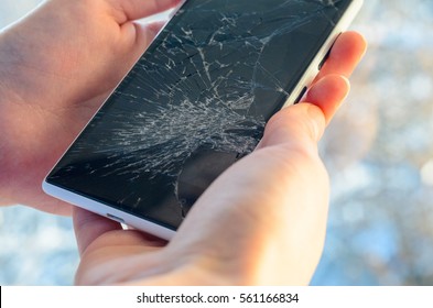 White Smartphone with broken screen in human hands on blured nature background