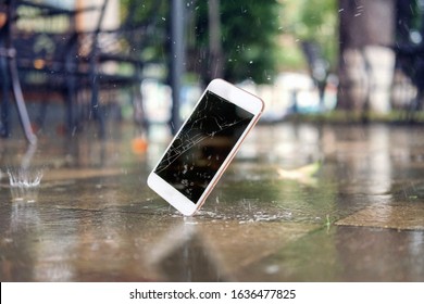 White smartphone falling and crashing on wet ground in the city park on a rainy day. accident with smartphone