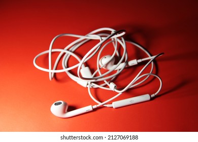 White smartphone headphones with a tangled cable line on a red background. Tangled white headphones close-up on a red background top view.