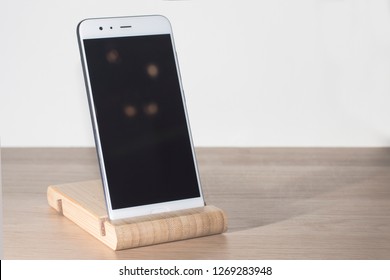White smartphone on a wooden stand is on the table. Copy space.