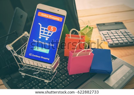 White smartphone runs an online shopping app put in a shopping cart on a laptop keyboard. Online shopping is the purchase of products and services on the internet that has become increasingly popular.