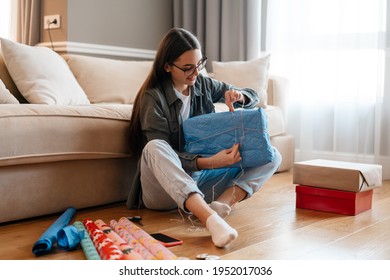 White smiling woman wrapping presents while sitting on floor at home - Powered by Shutterstock