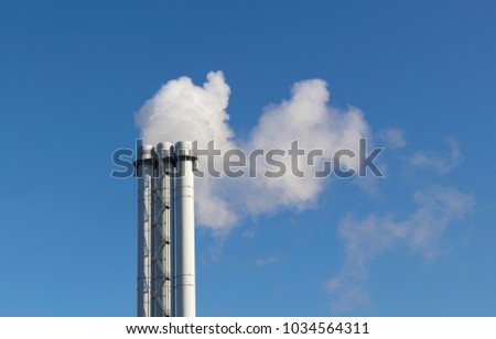 White smoke comes from a white chimney pipe on a background of blue sky.