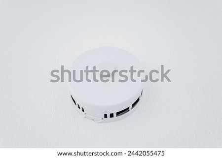 A white smoke detector is placed on a white surface, blending in seamlessly. The sleek design makes it a discreet yet important automotive lighting accessory for safety measures