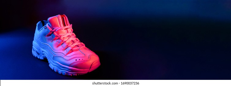 White Sneaker On Black Background In The Neon Red And Blue Light. Banner.
