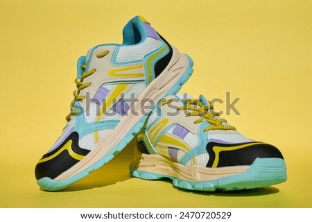 White sneakers with colored accents on yellow background, Pair of fashionable sport shoes. Studio shot of shoes for shop advertisement, creative minimalist style