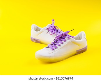 White Sneakers With Purple Laces On Yellow Background. Modern Minimal Fashion Art Trendy Bold Color Still Life