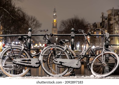 White snow covered bicycles parked on the bridge in winter, Blurred traditional houses and the Westerkerk tower, Prinsengracht, Amsterdam, Netherlands, Cycling is a common mode of transport in Holland