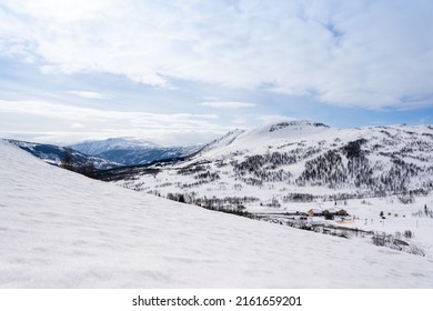 White snow-capped mountains in Norway over which there is a blue sky with soft puffy clouds