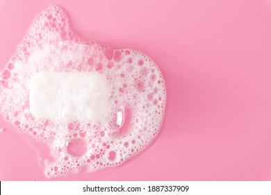 White soap bar and foam on pastel pink background. Flat lay, top view, copy space
