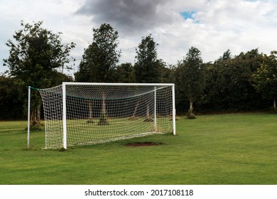 White Soccer Of Football Goal Post On A Grass Field Of A Training Ground. Dark Trees Background And Cloudy Sky