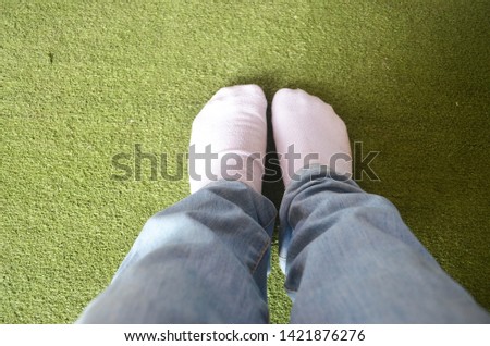 White socks under blue jeans worn by someone stepping on an artificial grass rug in green tone