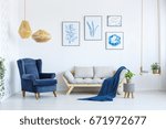 White sofa and blue armchair in living room with posters on the wall