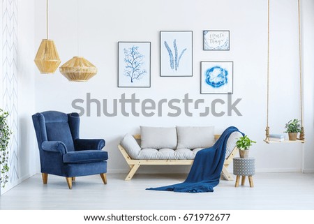 White sofa and blue armchair in living room with posters on the wall