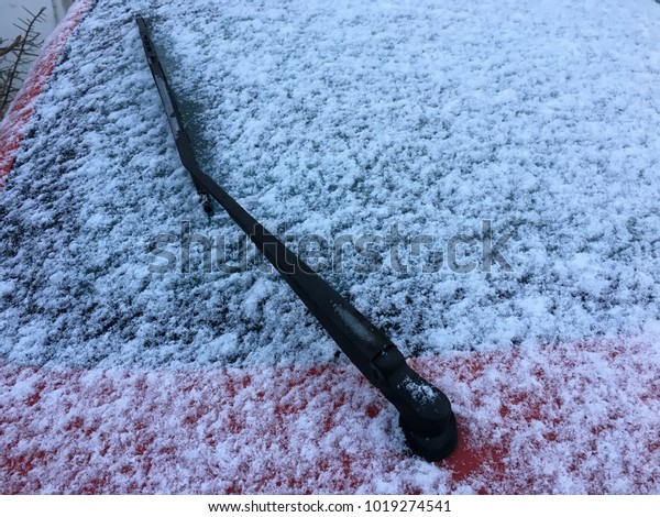 white soft snow collected on wind screen of a red\
car with a wiper arm\
exposed