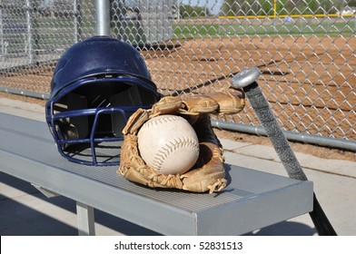 White Softball, Helmet, Bat, And Glove On An Aluminum Bench