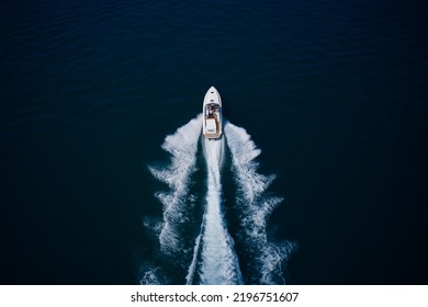 White Speedboat Fast Movement On Dark Water Top View. White Large Open Boat With People Moving Fast On Dark Blue Water Top View. White Speedboat Moving Up Aerial View.