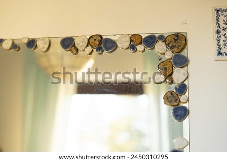 White sphere circular globe lantern lampshade hanging from bathroom ceiling light blue curtains in front of sunny window mirror yellow blue shell stone edge art on walls wooden window frame restroom