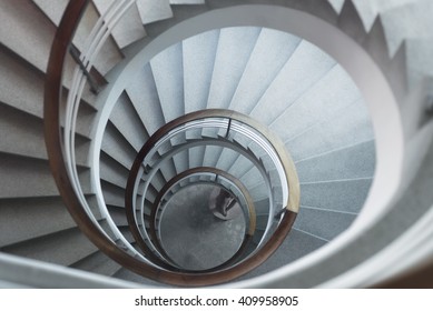 White spiral staircase in soft light with wooden banister looking down from above.