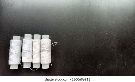 White spools of thread on a black background. Black card with texture, frame and sewing threads. Partial focus