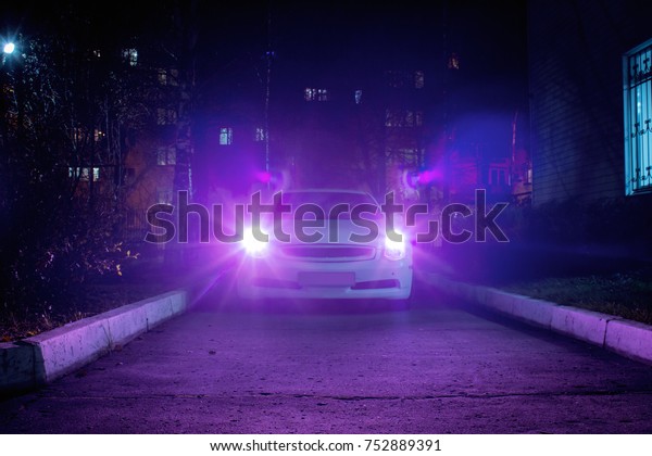 White sport car\
with pink headlights at\
night