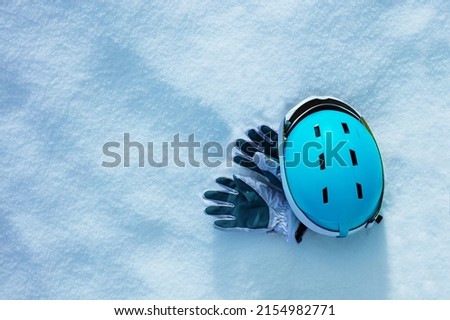 White sport gloves in the snow with blue ski helmet and mask, clean view from above, winter holidays concept