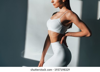 In white sportive clothes. Young caucasian woman with slim body shape is indoors at daytime. - Shutterstock ID 1937198329