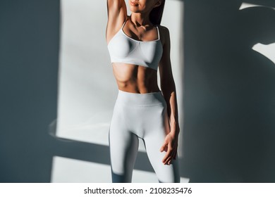 In white sportive clothes. Young caucasian woman with slim body shape is indoors at daytime. - Shutterstock ID 2108235476