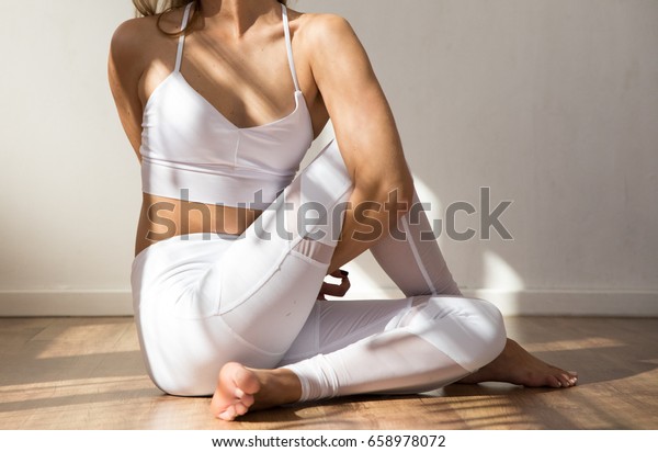 White sports bra and white\
yoga pants fitness outfit on a white background on a wooden floor\
in a modern studio space. warm morning light falling on the\
model