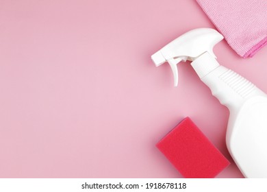White spray bottle for cleaning and cleaning rag with sponge on pink background.