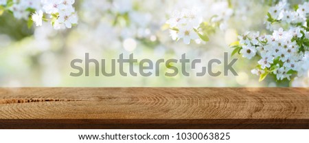 White spring flowers in a park with empty rustic wooden table for an easter background