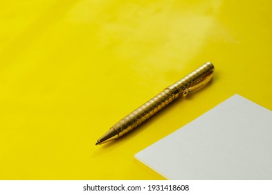 White Square Blank Tear-off Note Paper And Pen On Yellow Background. A Small Stack Of Paper Stickers And A Gold-colored Metal Pen On A Solid Background. No People.