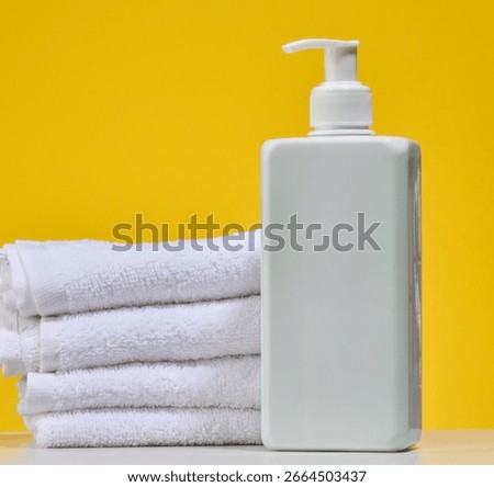 White square bottle with dispenser and stack of folded white towels, rich yellow background. Body care or spa treatment concept.