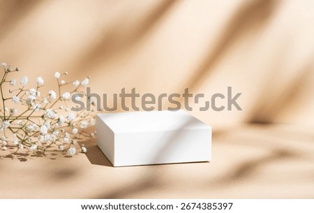 White square box on a beige background with gypsophila flowers and soft shadows. Concept abstract geometric design for advertising or product demonstration. Front view, copy space.