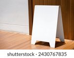 white square metal sign rests on a brick floor. The background is a wooden wall.